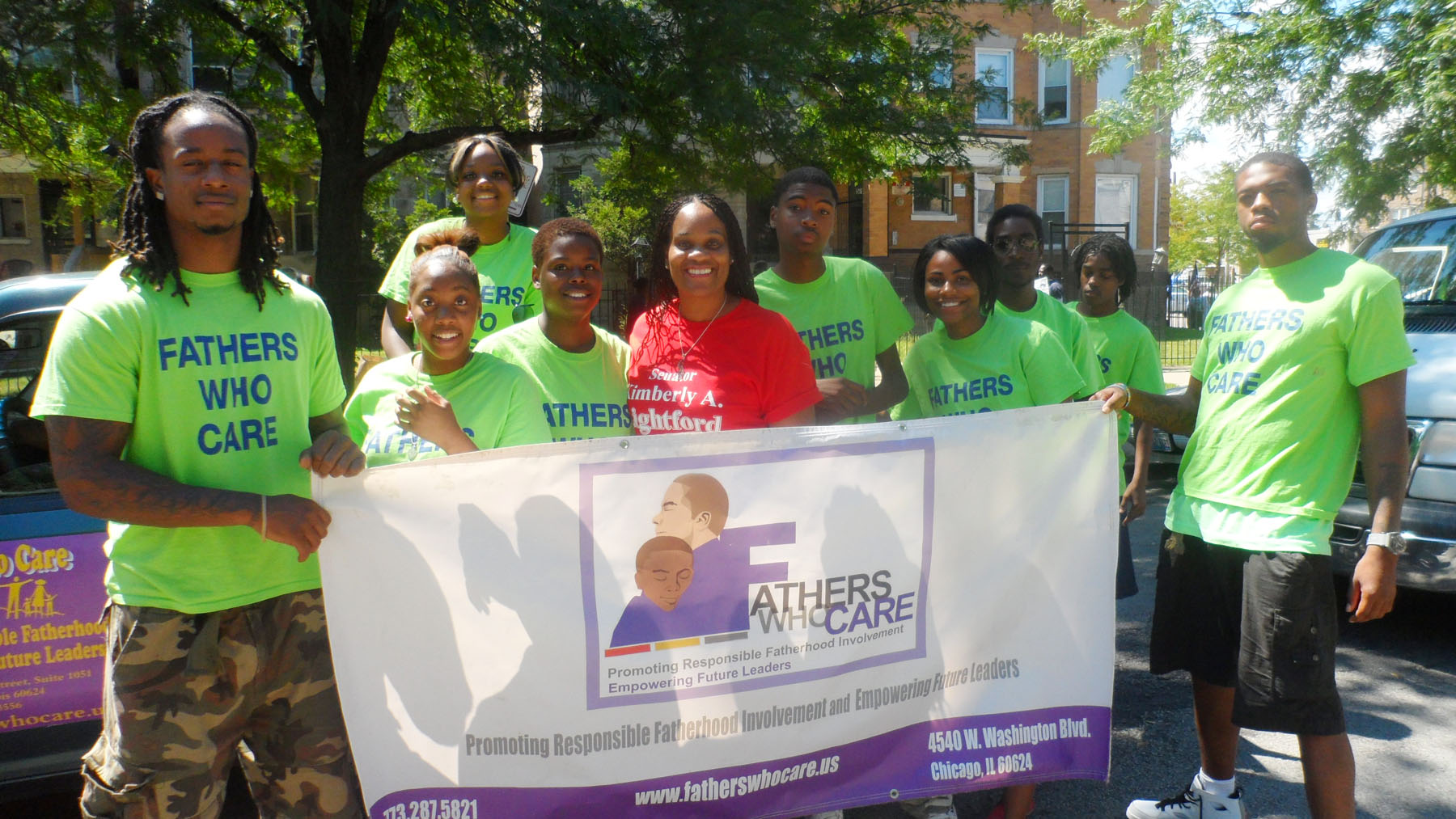 Young people and community leaders gathered around a Fathers Who Care service banner